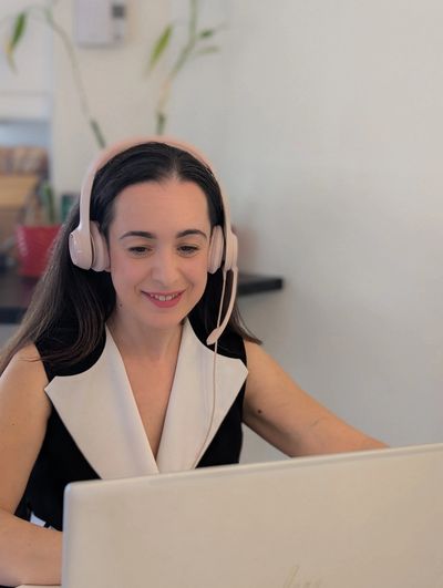 Woman wearing headset and smiling while working on a laptop.
