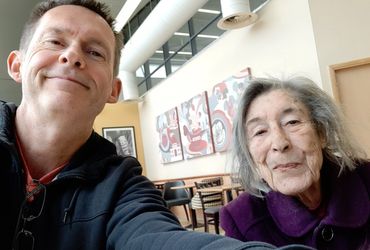 A man and an elderly woman take a selfie in a cozy cafe.