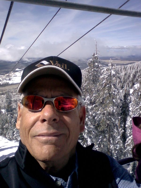 Man wearing sunglasses and a Vail cap on a ski lift.
