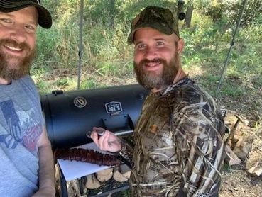 2 guys smoking meat in the outdoors.