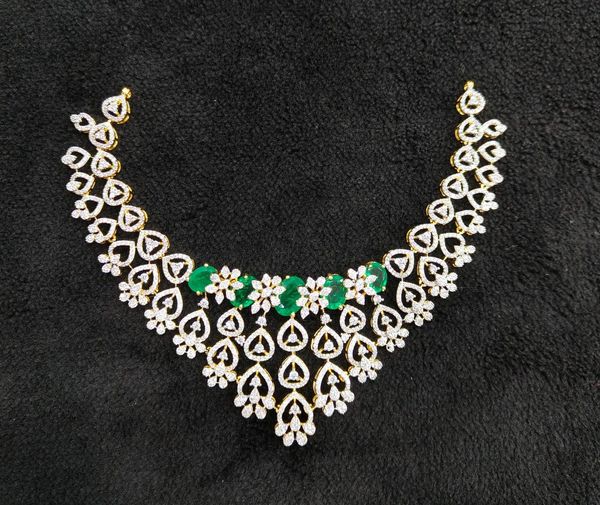 Intricate gold necklace with white diamonds and green gemstones on black fabric.