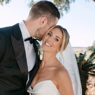 Groom kisses bride's forehead as she smiles joyfully on their wedding day.