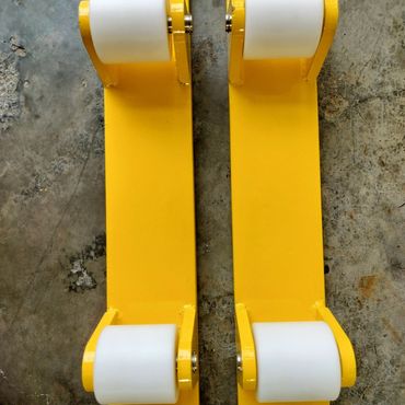 Two yellow metal brackets with white rollers on a rough floor.