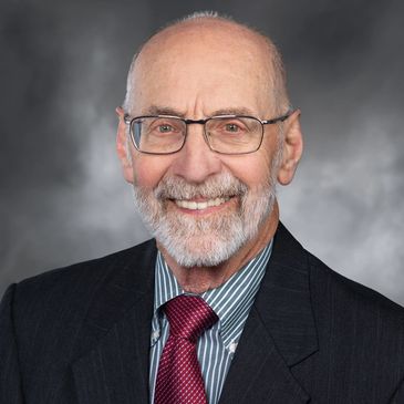 Elderly man with glasses in a suit smiling.
