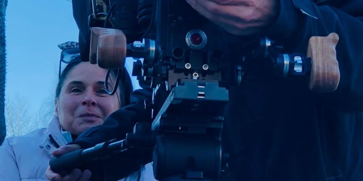 A woman and a person operating a professional camera outdoors.
