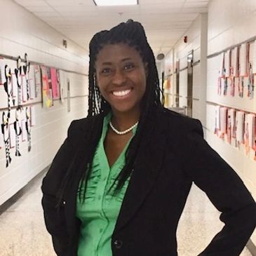 Smiling woman in hallway with a green blouse and black blazer.