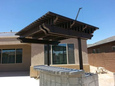 Modern backyard pergola with a stone bar counter under clear blue sky.