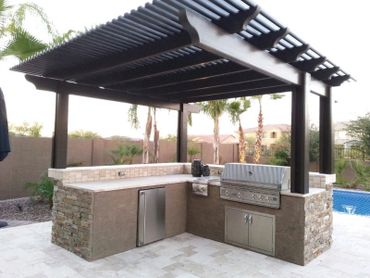 Modern outdoor kitchen with grill under a pergola beside a pool.