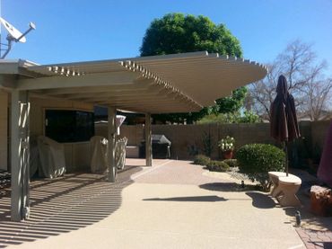 Backyard patio with covered seating area and plants under clear blue sky.