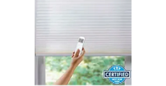 Hand controlling a white window blind with a remote control near a window.