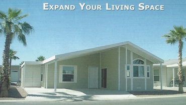 Modern manufactured home with carport and palm trees under a clear blue sky.
