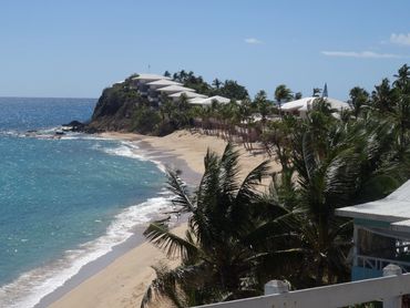 Seitenansicht des Curtain Bluff Hotel Antigua. Meer, Palmen und Gebäudekette am Hügel.