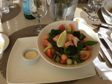 Lobstersalat in rundem tiefen Teller mit Tomaten, Brokkoli und Limone. Besteck und Gläser