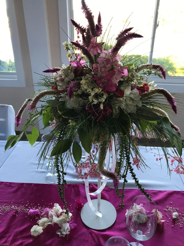 Tisch-Gesteck mit tropischen Blumen in Pink, Weiss und Grün in einem langen schmalen Ständer.