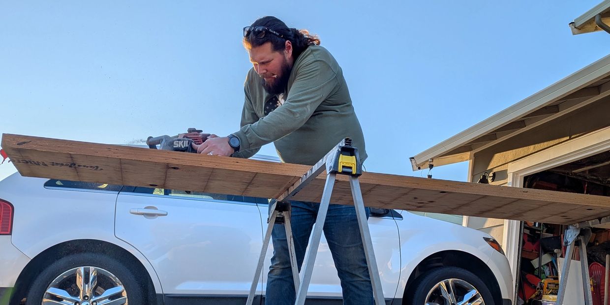 Man using a power saw on wood supported by sawhorses.