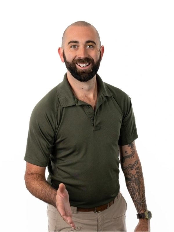 Smiling man with a beard and tattooed arm extending his hand for a handshake.