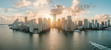 Sunset over a coastal city skyline with boats on the water.