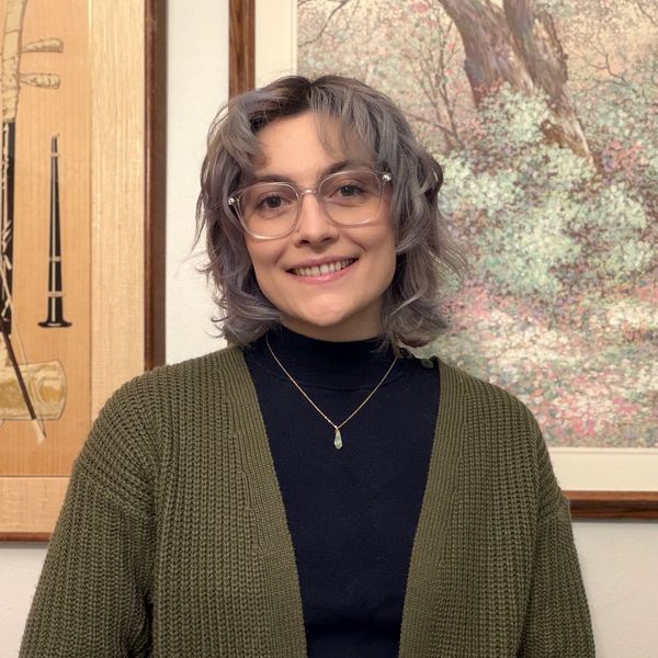 Smiling woman with glasses and curly hair, wearing a green cardigan and black top.