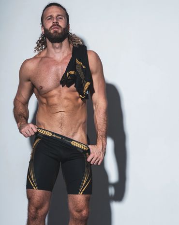 Muscular man posing in black and gold shorts.