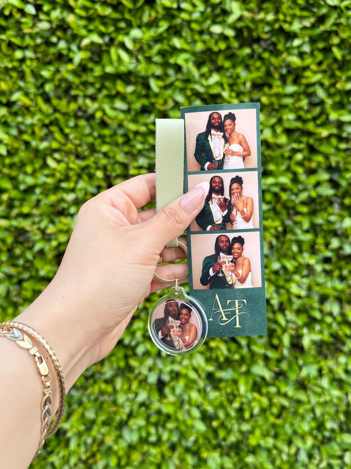 Hand holding a photo strip and keychain from a wedding with a green leaf background.