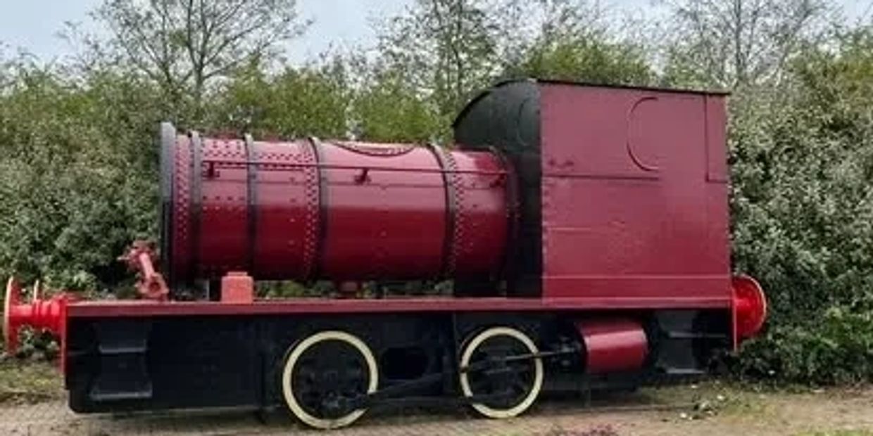 A small vintage red and black train engine outdoors near bushes.