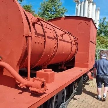 A red vintage train engine displayed outdoors with a person nearby.