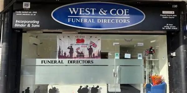 Exterior of West & Coe Funeral Directors with VE Day banner in the window.