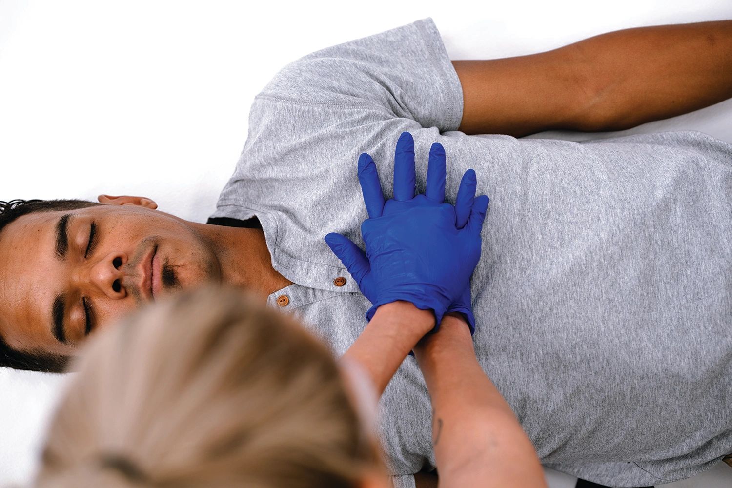 Person receiving CPR chest compressions from a gloved responder.