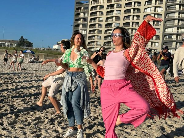 People dancing on a sunny beach with headphones on.