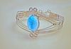 A large Larimar cabochon is wrapped in round sterling silver wire and mounted into a framework with tapering sides.