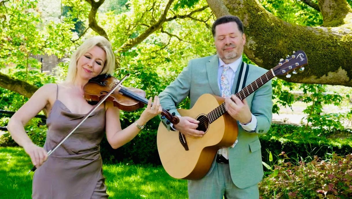 Violinist and Guitarist performing beneath a tree