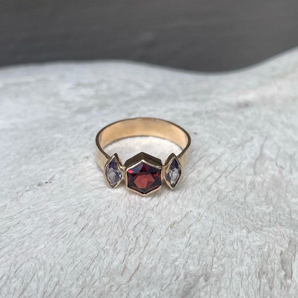 A gold filled ring with a garnet center stone and two azurite stones on the side
