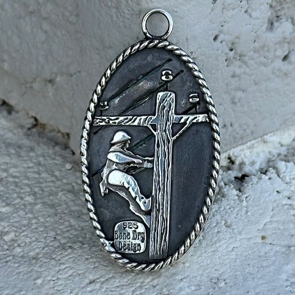 A custom pendant with the back designed with a Lineman working on a power line pole.