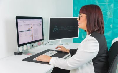 Professional woman working on spreadsheets at her desk with dual monitors.