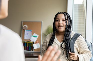 Young woman with braided hair and backpack talking indoors.