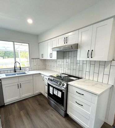 Modern white kitchen with stainless steel stove and dark handles.