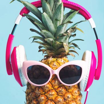 Pineapple wearing pink sunglasses and headphones against a blue background.