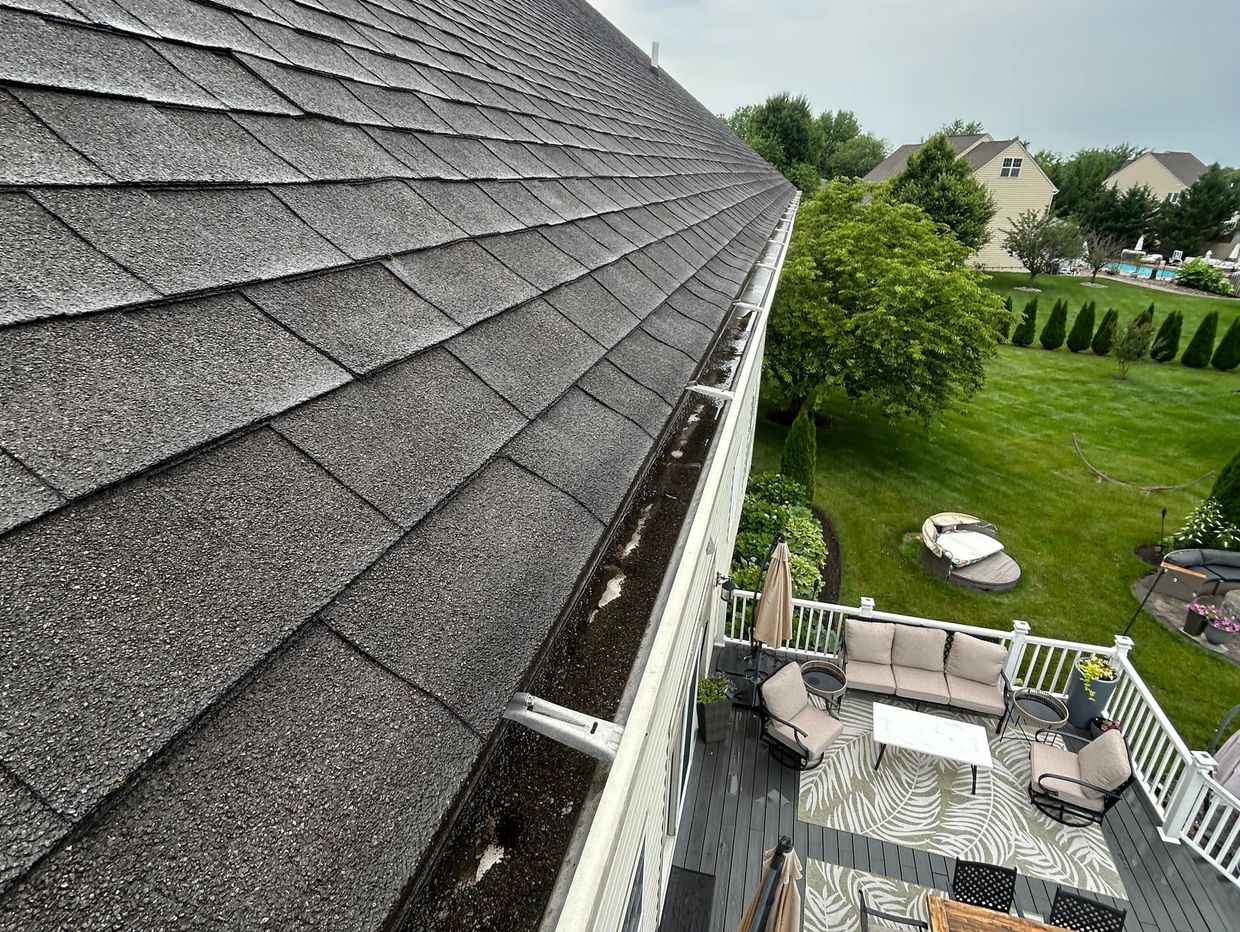 View of a house roof, patio, and backyard with green lawn.