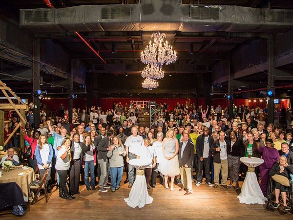 Large group of people posing together in an indoor event space with chandeliers.