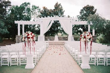 wedding ceremony at Royal Crest Room with white urns and white columns with red and white flowers