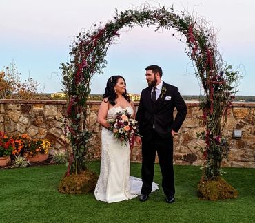 Garden Arch in burgundy with bride and groom holding hands and the bride is holding her bouquet