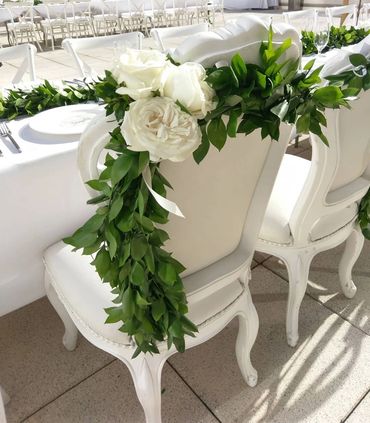 white rose reception chair garland on white leather chairs at an outdoor wedding reception table