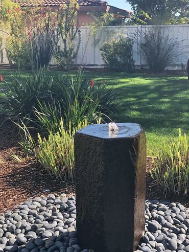Basalt column water feature bubbling over smooth Mexican Pebbles in a modern garden landscape.