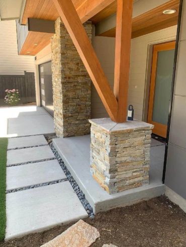 Modern house entrance with stone pillars and wooden beams.
