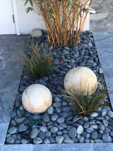 Decorative garden bed with rocks, plants, and spherical stones.