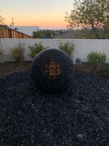 Spherical fire pit in a backyard at sunset.