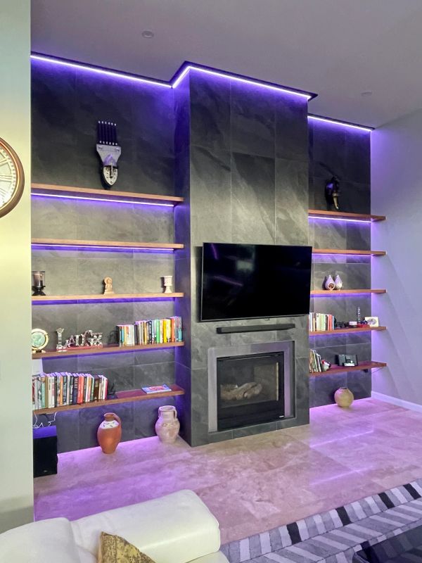 Modern living room with purple LED-lit shelves and fireplace.