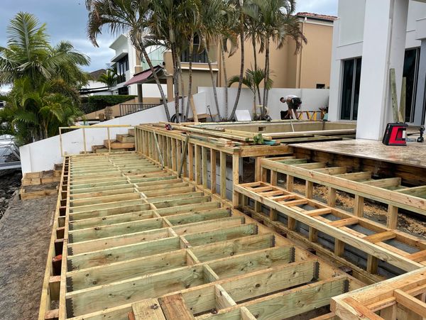 Wooden deck construction near modern houses with palm trees.