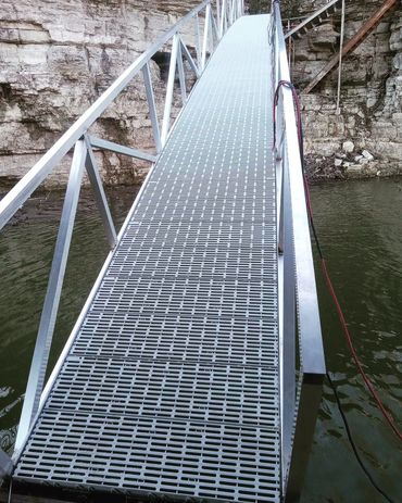 A metal bridge over water with rocky cliffs in the background.