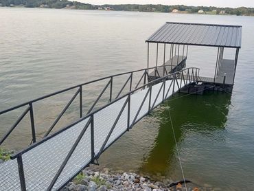 Metal walkway leading to a covered dock on a calm lake.